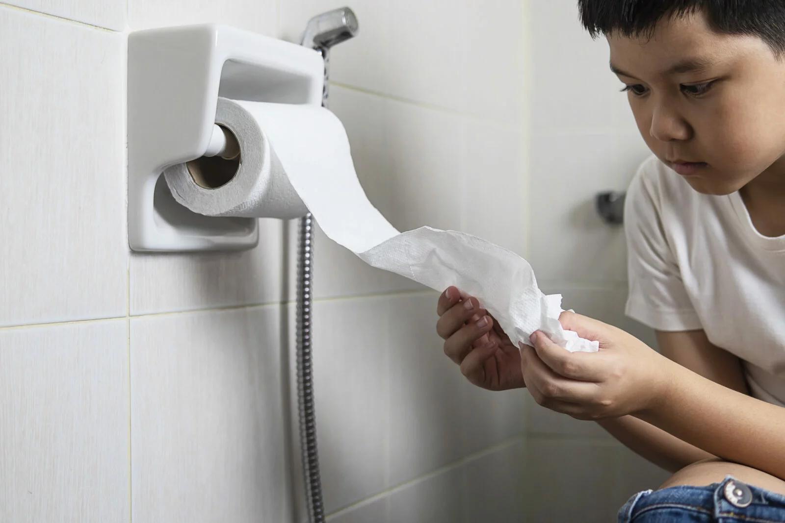 Asian boy sitting on toilet bowl holding tissue paper  - health problem concept